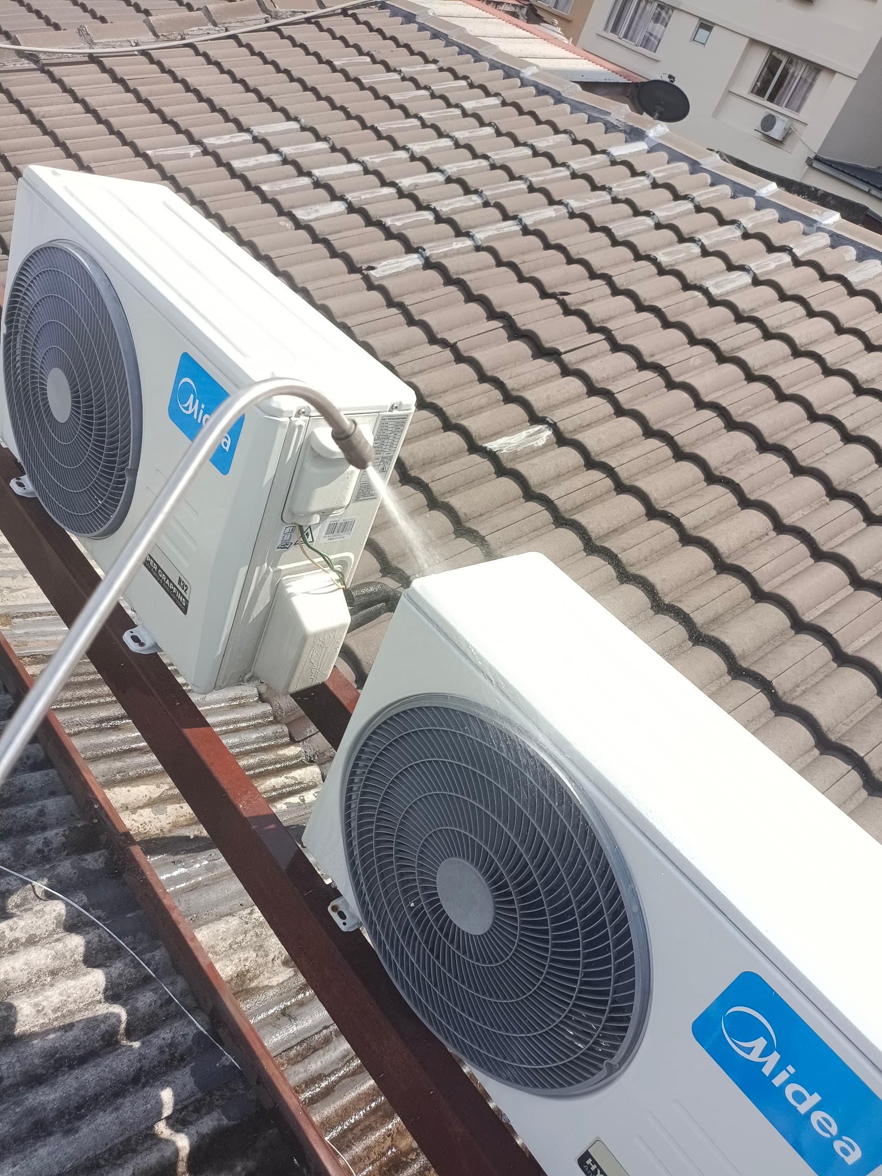 Technician rinsing two outdoor aircon units with a spray lance during a service visit