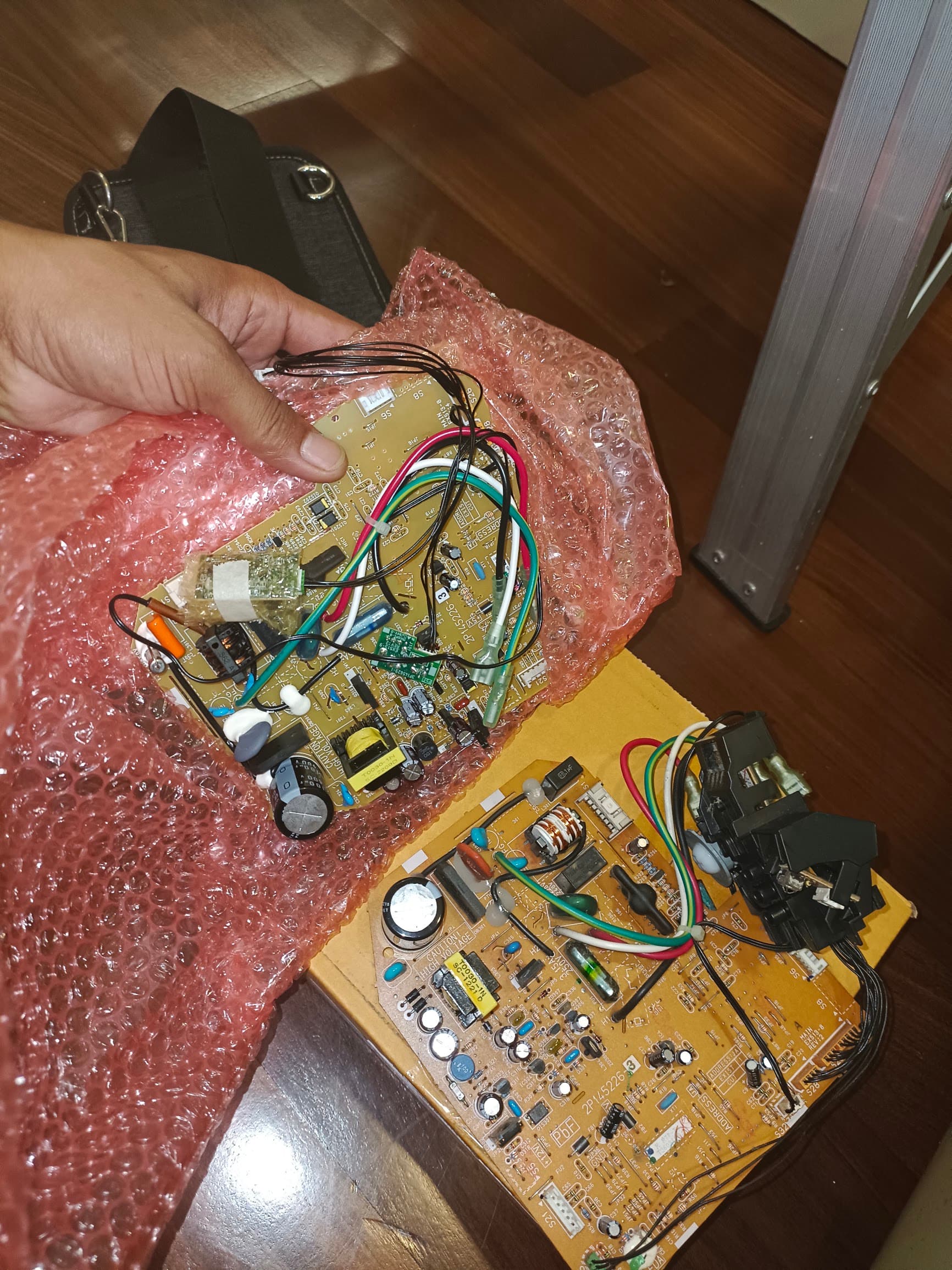 Two replacement aircon control boards in bubble wrap, held by a technician before fitting